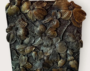 May include: A rectangular, bronze-colored wall sconce featuring a detailed floral design. The flowers are intricately sculpted, with a textured background. The base of the sconce has a rectangular shape with a light source.