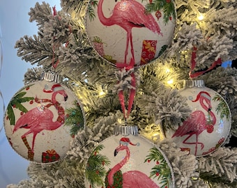 Può includere: Quattro palline di Natale a forma di fenicottero rosa con sfondo bianco e finitura scintillante. Le palline raffigurano un fenicottero che indossa un cappello da Babbo Natale e tiene un regalo. Le palline sono decorate con palme, regali e bastoncini di zucchero.