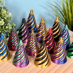 May include: A collection of 12 iridescent, spiral-shaped, cone-shaped ornaments in various colors, including gold, blue, green, purple, and red. The ornaments are arranged on a wooden surface.