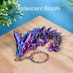 May include: A iridescent purple and blue crystal keychain with a silver key ring. The keychain is shaped like a cluster of crystals and has the text "Iridescent Bloom" on the background.