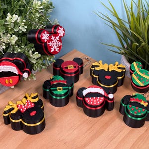 May include: A collection of eight black plastic keychains shaped like mouse heads, featuring various holiday-themed designs including Santa hats, reindeer antlers, elf outfits, and snowflake patterns in red, green, gold, and white colors.