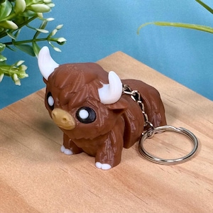 May include: A brown and white fuzzy keychain shaped like a highland cow with a silver key ring.