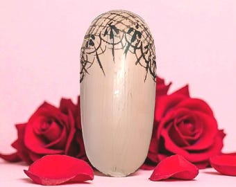 May include: A light beige, oval decorative object with a black, web-like design on the top. The object is set against a pink background with red rose petals and two red roses.