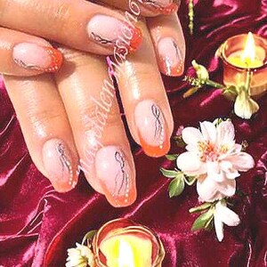 May include: Close-up of manicured nails with a French tip design. The nails have a light pink base, orange tips, and silver and black abstract art. The image also includes lit candles and flowers.