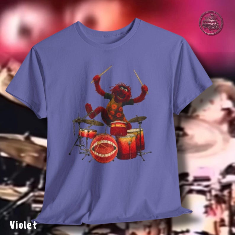 K&ouml;nnte beinhalten: Violettes T-Shirt mit einer Zeichentrickfigur, die ein Schlagzeug spielt. Die Figur ist rot mit gelben und orangen Akzenten. Das Schlagzeug ist rot und orange. Das Wort "Violet" ist unten auf dem T-Shirt aufgedruckt.