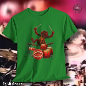 K&ouml;nnte beinhalten: Irisch gr&uuml;nes T-Shirt mit einer Zeichentrickfigur, die Schlagzeug spielt. Die Figur ist rot mit einem gelb-braun gemusterten Hemd. Das Schlagzeug ist rot und orange. Der Text "Irish Green" steht unten.