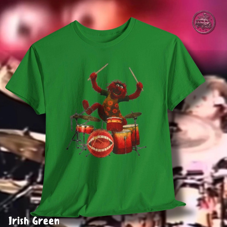 K&ouml;nnte beinhalten: Irisch gr&uuml;nes T-Shirt mit einer Zeichentrickfigur, die Schlagzeug spielt. Die Figur ist rot mit einem gelb-braun gemusterten Hemd. Das Schlagzeug ist rot und orange. Der Text "Irish Green" steht unten.