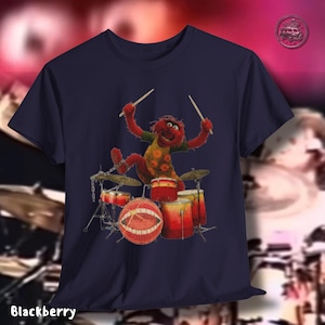 K&ouml;nnte beinhalten: Marineblaues T-Shirt mit einem Cartoon-Bild von Animal von den Muppets, der Schlagzeug spielt. Animal ist rot mit einem gr&uuml;nen und orangefarbenen Hemd und h&auml;lt Trommelst&ouml;cke. Das Schlagzeug ist rot und gelb. Das Wort "Blackberry" ist unten aufgedruckt.