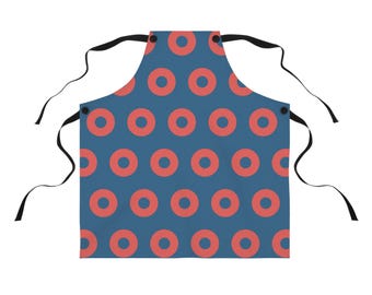 May include: A blue apron with a repeating pattern of coral-colored circles. The apron has black ties at the neck and waist. The apron is made of a durable fabric.