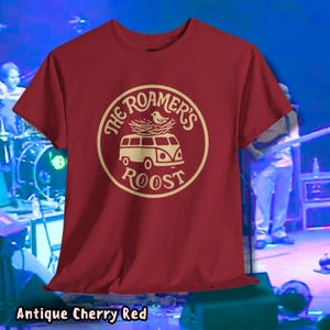 May include: Antique cherry red t-shirt with a circular graphic. The graphic features a vintage van with a bird and nest on top, encircled by the words "The Roamer's Roost". The shirt's color is described as "Antique Cherry Red".