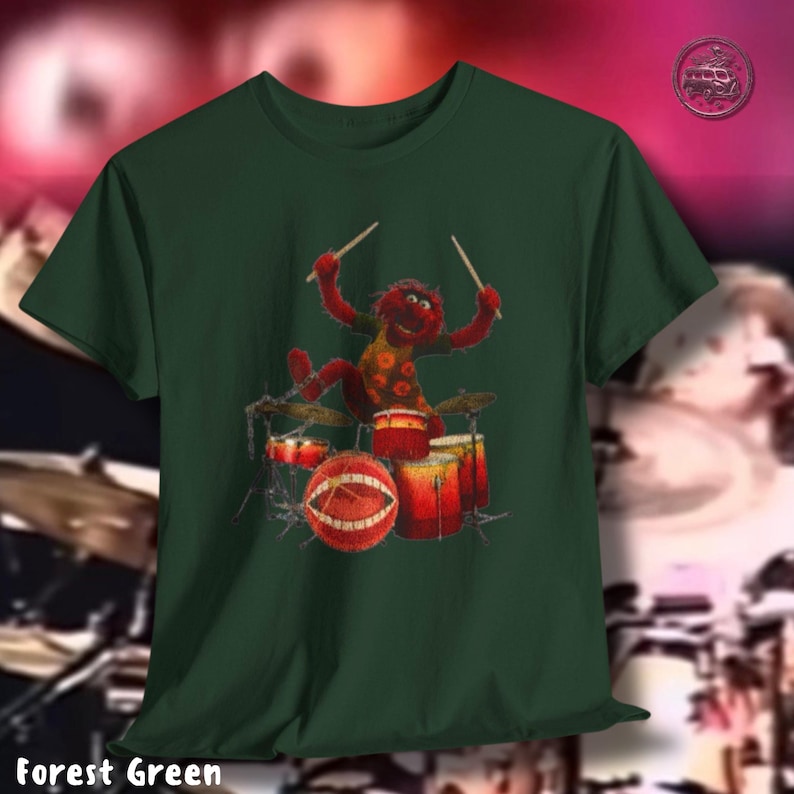 K&ouml;nnte beinhalten: Forstgr&uuml;nes T-Shirt mit einer Zeichentrickfigur, die Schlagzeug spielt. Die Figur ist rot mit gelben und orangen Details. Das Schlagzeug ist rot und orange. Der Text "Forest Green" befindet sich am unteren Rand des T-Shirts.