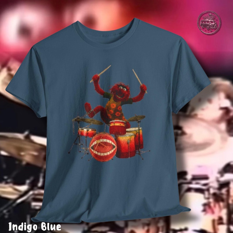 K&ouml;nnte beinhalten: Indigoblaues T-Shirt mit einer Zeichentrickfigur, die Schlagzeug spielt. Die Figur ist rot mit einem gelb-orange gemusterten Hemd. Das Schlagzeug ist rot und orange. Der Text "Indigo Blue" befindet sich am unteren Rand des T-Shirts.