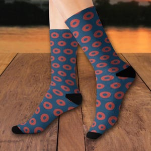 May include: A pair of blue socks with a repeating pattern of orange oval shapes. The socks have black heels and toes. The background is a wooden surface with an orange and yellow sky.