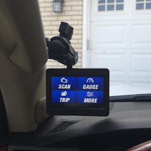 May include: A black digital display screen mounted on a car dashboard. The screen shows blue boxes with white text: SCAN, GAUGE, TRIP, and MORE. The display is mounted with a black bracket.