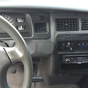 Può includere: Vista interna del cruscotto di un veicolo, con volante grigio, tachimetro e comandi radio. Il cruscotto è principalmente grigio con dettagli neri, tra cui bocchette dell'aria e un impianto stereo.