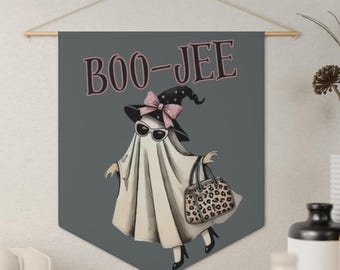 May include: A gray wall hanging banner featuring a ghost wearing a black witch hat with a pink polka dot bow, sunglasses, and black heels, carrying a leopard print handbag. The text BOO-JEE is printed in a dark pink font above the ghost illustration.