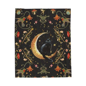 May include: A black blanket featuring a black cat sitting on a crescent moon. The blanket has a dark background with a repeating pattern of hummingbirds, flowers, stars, and moths. The moon is gold with intricate details.
