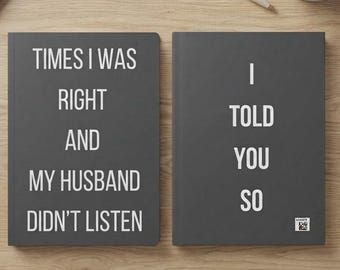 May include: Two dark gray notebooks with white text. The left notebook reads: TIMES I WAS RIGHT AND MY HUSBAND DIDN'T LISTEN. The right notebook reads: I TOLD YOU SO. Both notebooks have a clean, rectangular design with a matte finish and white lettering.