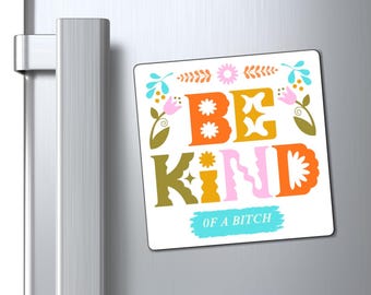 May include: A white square magnet with the words "BE KIND OF A BITCH" in colourful, retro-style lettering. The design includes floral and star accents, and is displayed on a refrigerator.