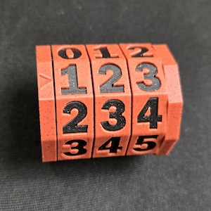 May include: A red, textured, four-sided, rotating number cube with black numbers 012345.