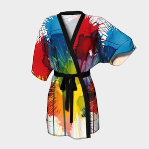 Może przedstawiać: Kolorowy szlafrok w stylu kimono z żywym abstrakcyjnym wzorem. Szlafrok posiada czarny pasek i wykończenia oraz jest ozdobiony plamami czerwonej, niebieskiej, żółtej i zielonej farby. Szlafrok jest wykonany z lekkiej tkaniny.