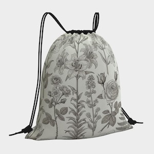 May include: A drawstring backpack featuring a botanical floral print in shades of gray and white. The design includes detailed illustrations of lilies, roses, and other flowers. The bag has black drawstrings and a black top.