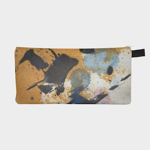 May include: A rectangular pencil case with a colorful abstract design. The case features a tan background with black, blue, and pink paint splatters. A black zipper pull is attached to the side.