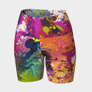 May include: High-waisted athletic shorts with a vibrant abstract paint splatter design. The shorts feature a mix of bright colors including pink, orange, green, blue, and yellow. The fabric appears to be a smooth, stretchy material.
