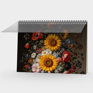 Könnte beinhalten: Ein Spiral-Kalender mit einem lebendigen Blumenstillleben. Das Kunstwerk zeigt Sonnenblumen, Gänseblümchen, Mohnblumen und andere Blumen in einer reichen, farbenfrohen Anordnung vor dunklem Hintergrund. Der Kalender ist geöffnet und zeigt das Kunstwerk.