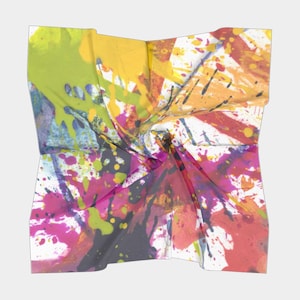 May include: A square scarf with a vibrant abstract design. The scarf features a white background with colorful paint splatters in shades of yellow, green, pink, orange, and black. The fabric is folded and twisted, creating a dynamic visual effect.