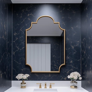 Può includere: Interno bagno con mobile lavabo bianco, rubinetteria dorata e specchio con cornice dorata. Le pareti sono blu scuro con effetto marmoreo. Due vasi con fiori bianchi sul piano. Design moderno ed elegante.