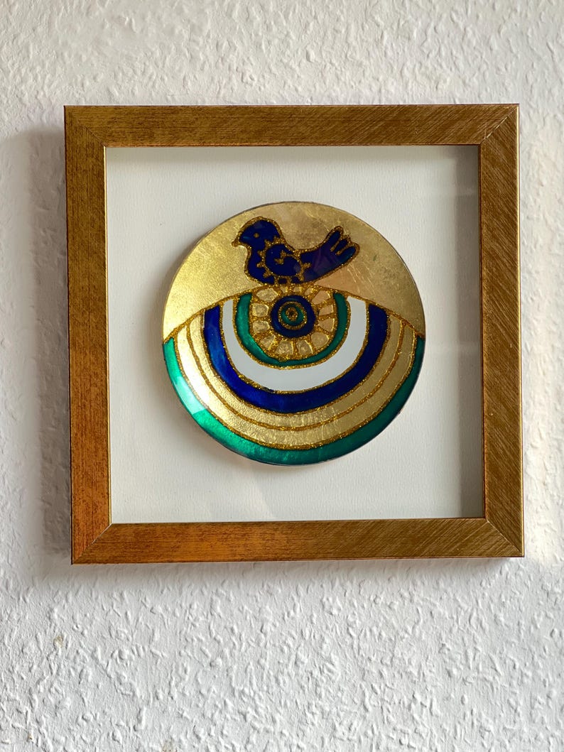 Pode incluir: Prato decorativo emoldurado com fundo dourado e desenho de p&aacute;ssaro azul. O prato apresenta an&eacute;is conc&ecirc;ntricos verdes, brancos e azuis, e est&aacute; envolto em uma moldura de madeira dourada. A obra de arte &eacute; exibida em um fundo branco.