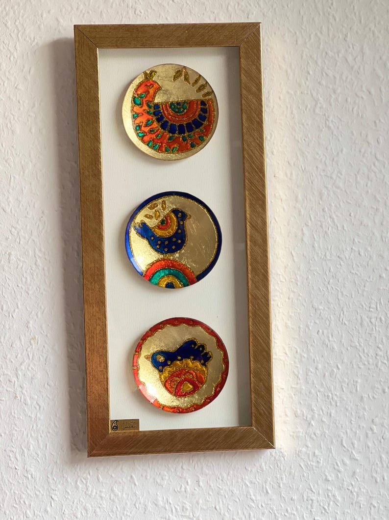 Pode incluir: Uma obra de arte emoldurada com tr&ecirc;s pequenos pratos decorativos redondos. Cada prato tem um fundo dourado com desenhos coloridos de p&aacute;ssaros em vermelho, azul, laranja e verde. A moldura &eacute; de cor dourada quente.
