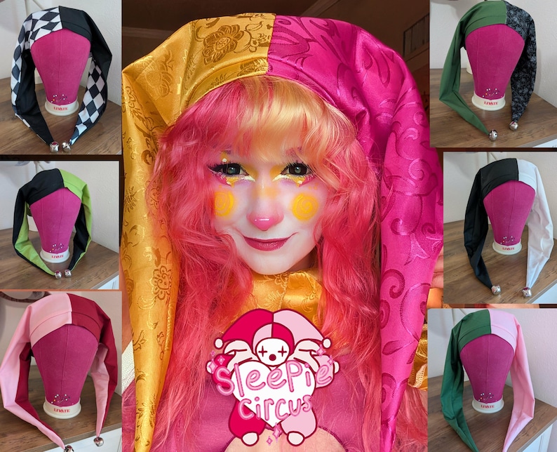 May include: A collection of colorful jester hats in various color combinations, including black and white checkered, pink and gold, and green and black. Each hat has long, pointed ends with a small silver bell at the tip. The hats are displayed on pink mannequin heads.