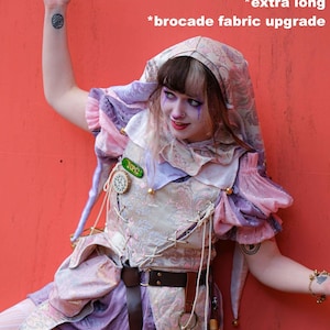 May include: A whimsical costume featuring a hooded top with brocade fabric, a laced bodice, and layered sleeves in shades of pink, purple, and cream. The outfit includes a brown belt, a decorative pin, and a small pouch. The text on the image says "extra long" and "brocade fabric upgrade".