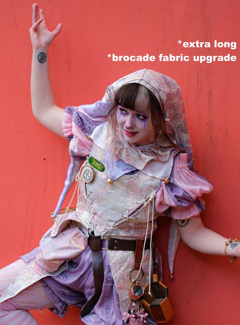 May include: A whimsical costume featuring a hooded top with brocade fabric, a laced bodice, and layered sleeves in shades of pink, purple, and cream. The outfit includes a brown belt, a decorative pin, and a small pouch. The text on the image says "extra long" and "brocade fabric upgrade".