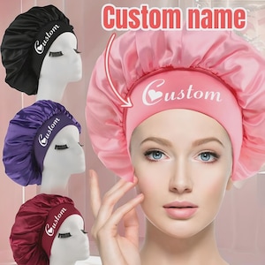 Puede incluir: Gorros de dormir de satén en negro, morado y burdeos, con un gorro rosa en primer plano. Cada gorro presenta la palabra "Custom" en escritura blanca. El gorro rosa tiene el texto "Custom name" encima.