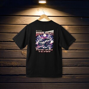 May include: Black t-shirt with a white car graphic and the text "BURN OUT!!!" in pink and purple. The text "燃え尽きる" is in Japanese above the graphic. The text "RACING TEAM" is below the graphic.