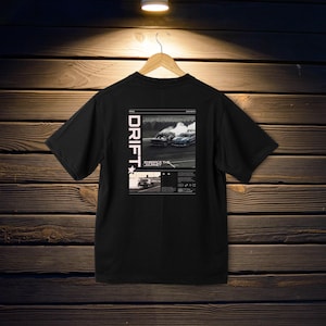 May include: Black t-shirt with a graphic design featuring the word "DRIFT" in white vertical text on the left side. The back of the shirt displays a black and white image of two cars drifting, with the text "EMBRACE THE JOURNEY".