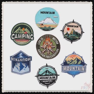 May include: A selection of embroidered patches featuring outdoor and camping motifs. Designs include mountains, campfires, and the text "Camping", "Mountain", and "Life is Better Around the Campfire". Patches are in various shapes and colours.