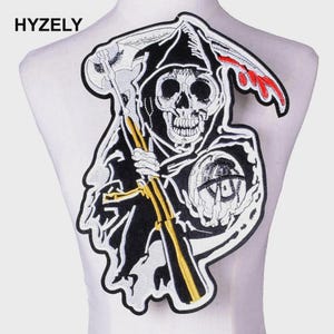 Op de afbeelding: Geborduurde patch met een Grim Reaper schedel ontwerp, met een zeis en een cirkelvormig embleem. De patch is voornamelijk zwart en wit met gouden en rode accenten. De tekst "HYZELY" is bovenaan zichtbaar.