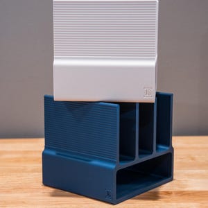 May include: A two-piece desk organizer set. The top piece is white with horizontal ridges, and the bottom piece is navy blue with vertical ridges and multiple compartments. Both pieces have a small "JG" logo.