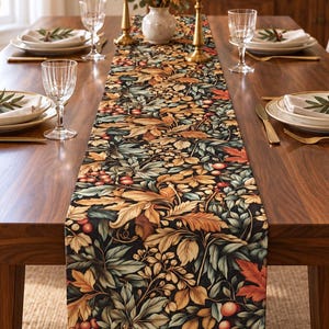 May include: A long rectangular table runner featuring a dense botanical print of autumn leaves, berries, and foliage in shades of orange, gold, deep green, and brown on a dark background, centred on a wooden dining table with place settings.