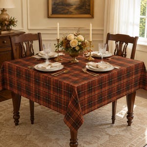 Peut inclure: Une table à manger carrée recouverte d'une nappe à carreaux rouille, marron et noir. La table est dressée avec des assiettes blanches, des serviettes pliées, des verres transparents, des couverts dorés, deux bougies et un centre de table floral.