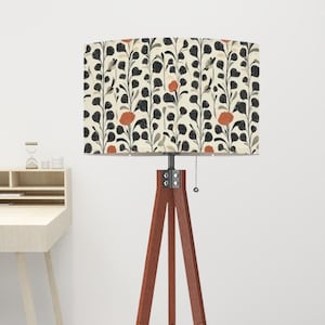 May include: A wooden tripod floor lamp with a rectangular lampshade. The lampshade features a cream background with a repeating pattern of black leaves, orange flowers, and gray accents. The lamp has a pull chain.