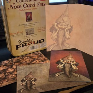 May include: Collectible note card sets featuring an illustration of a gnome with a long beard and pointed hat. The set includes a tin, cards, and envelopes. The tin reads "Oddly Familiar Gnome" and "World Froud".