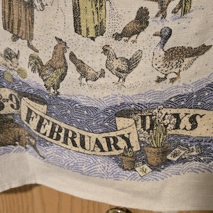 May include: A linen fabric with a Groundhog Day theme. The design features various farm animals, including chickens, ducks, and rabbits, along with the text "February" and "28 or 9 Days". The color palette includes beige, blue, and brown.