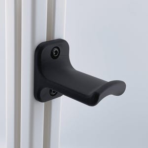 Puede incluir: Un tirador de puerta negro con un agarre curvo está montado en un marco de puerta blanco. El tirador se fija con dos tornillos. El diseño es moderno y minimalista.