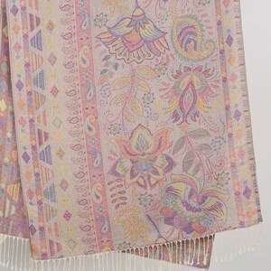 May include: A beige scarf with a detailed floral pattern in shades of pink, yellow, and purple. The design includes paisley and geometric elements. The scarf has a fringed edge.