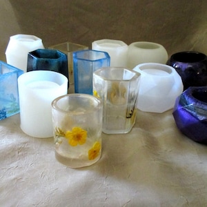 May include: Assortment of clear, white, blue, and purple resin candle holders in various shapes, including square, round, and hexagonal. Some holders feature pressed flowers.